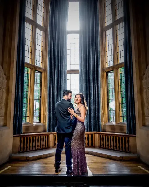 Couple poses with big wooden windows at the back.