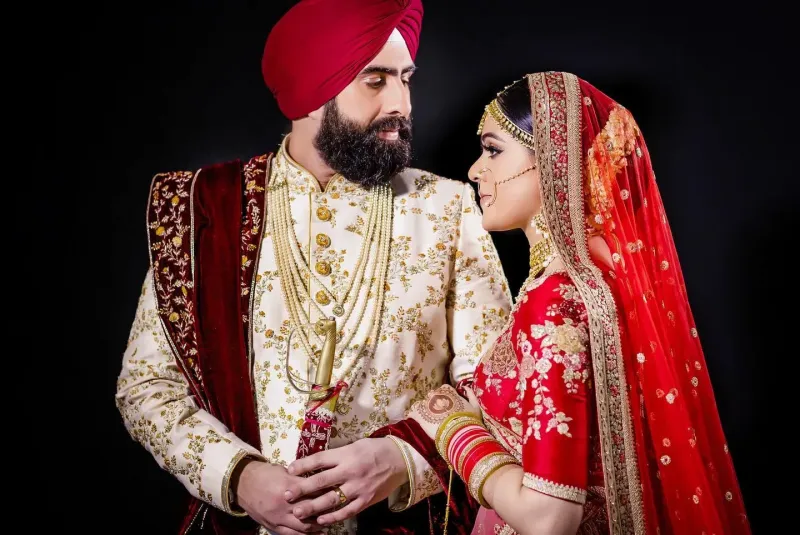 Traditional Sikh couple attire, Groom with sherwani and Bride with stunning red lehenga holding the hand of the Groom.