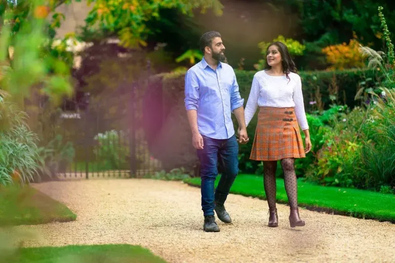 Couple holding hands walking in a lush green garden in London.