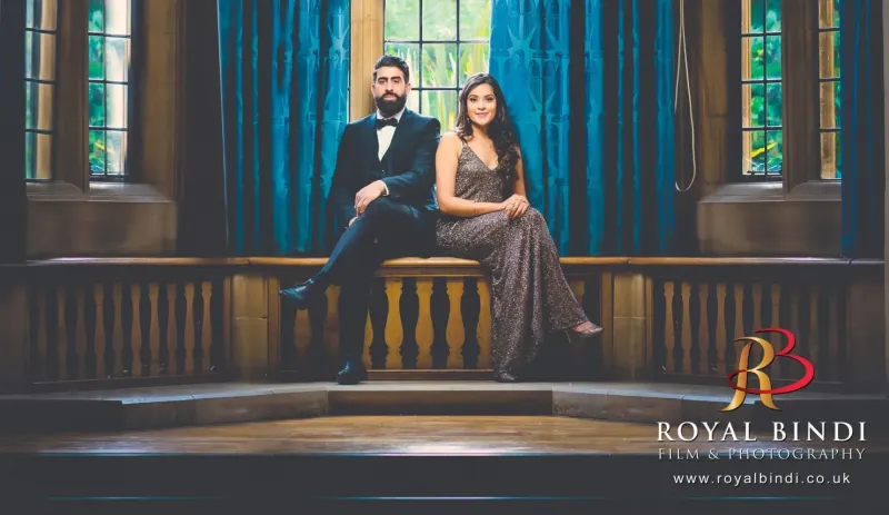 Bride and Groom sitting on a wooden bench with windows and blue curtains behind them.