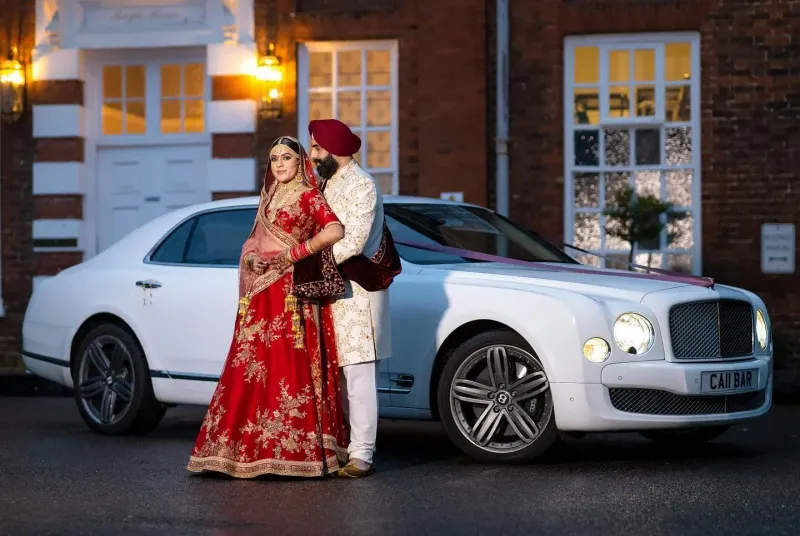 Couple\'s Sikh wedding photography with their traditional wedding attire and a luxury white car behind them.