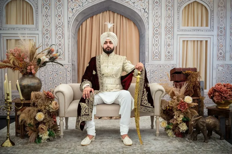 Sikh groom sitting on a sofa holding a Sikh sword in his hand.