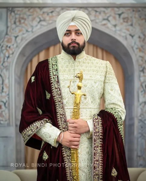 Sikh groom standing holding Sikh sword in his hand.