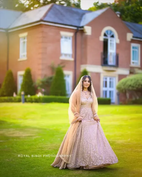 Bride\'s candid moment in a garden with a red building at her back.