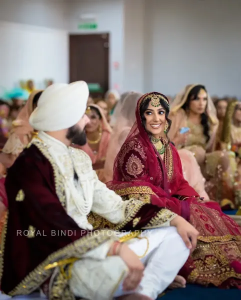 Sikh couple looking at each other, bride passinf smilling on the Anand karaj ceremony day.