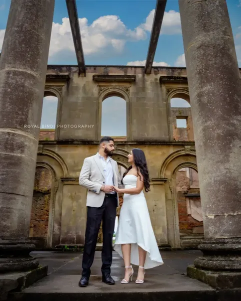 Coupke holding hands in front of two gaint pillars at a historic place in London.