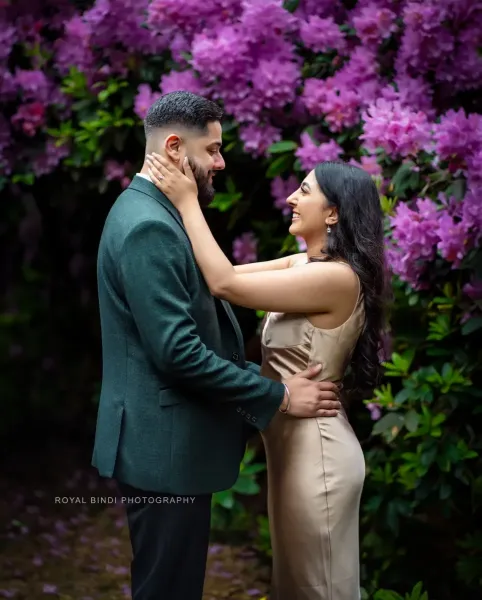 Couple looking at each other with love in front of purple flower tree in a garden.