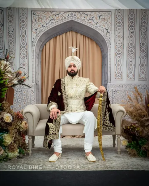 Sikh groom sitting on a chair with flowers arround him, holding a Sikh sword in his hand.