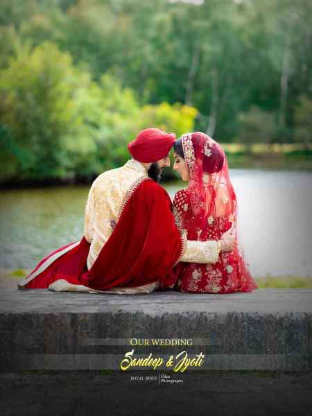 A couple embracing in traditional wedding attire by a serene lake, surrounded by lush greenery.