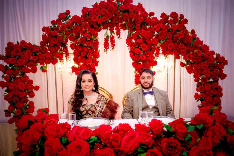 Pavan and Rajan reception moments sitting with red flowers on their background and on the table.