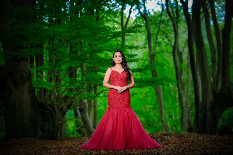 Bridal pre-wedding photoshoot, bridal wearing red dress standing with green trees at her back.