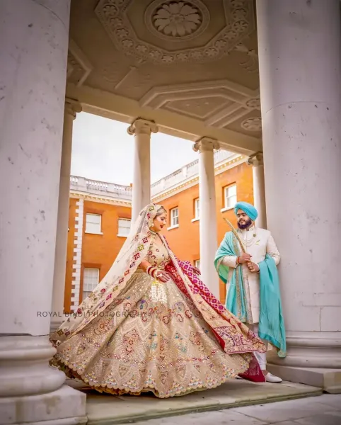 Ramita and Amrit in a stunning Sikh wedding portrait under architectural columns, showcasing traditional attire and elegance.