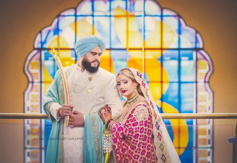 Sikh wedding couple standing with a Grudwara big frame at the back.