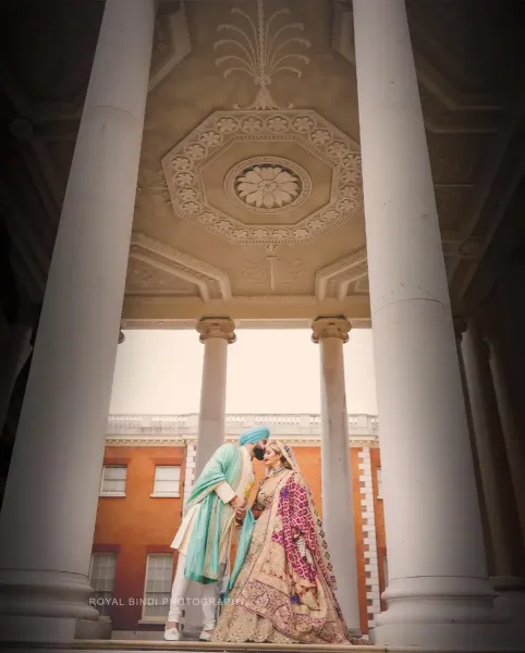 Sikh wedding couple\'s portrait under architectural pillars.