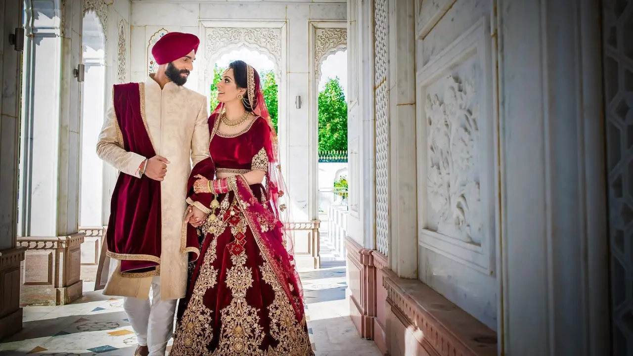 Sikh bride and groom in traditional attire walking hand in hand at Sri Guru Nanak Darbar Gurdwara in Gravesend, with elegant white marble architecture in the background.