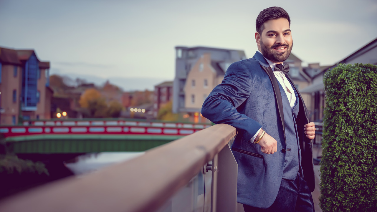 Man in a blue tuxedo leaning on a railing