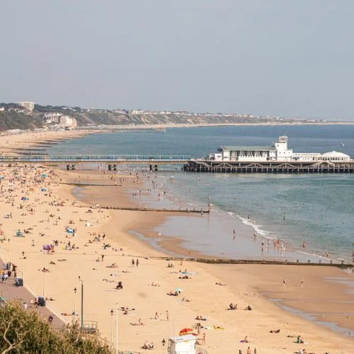 A view of Bournemouth Beach with people relaxing on the sandy shore and Bournemouth Pier in the background.