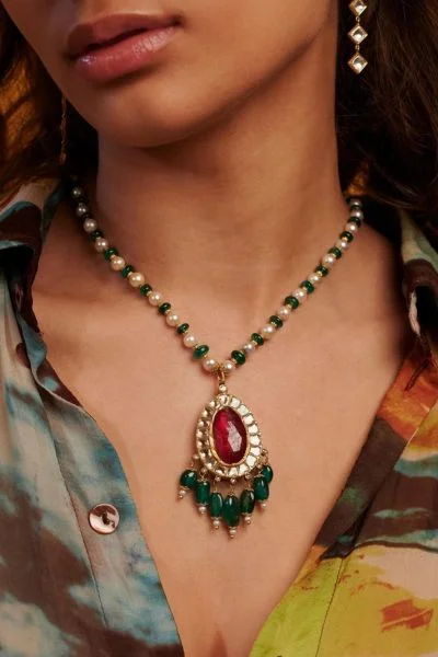 Woman wearing a gold necklace with a large ruby stone and green emerald beads