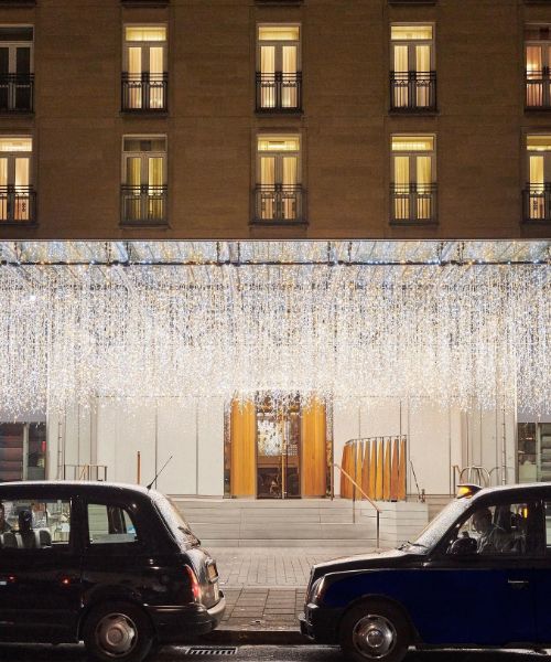 A photo of the Berkeley Hotel entrance in London at night. The hotel is adorned with twinkling lights above the entrance, and two black London taxis are parked in front.