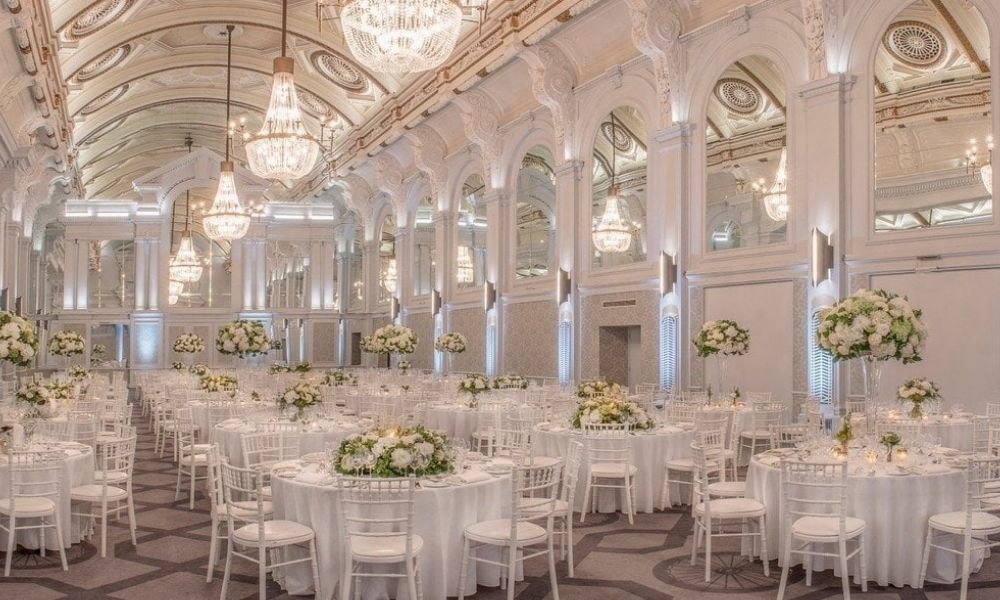 A photo of a grand ballroom with high ceilings, ornate chandeliers, and round tables set for a formal event.