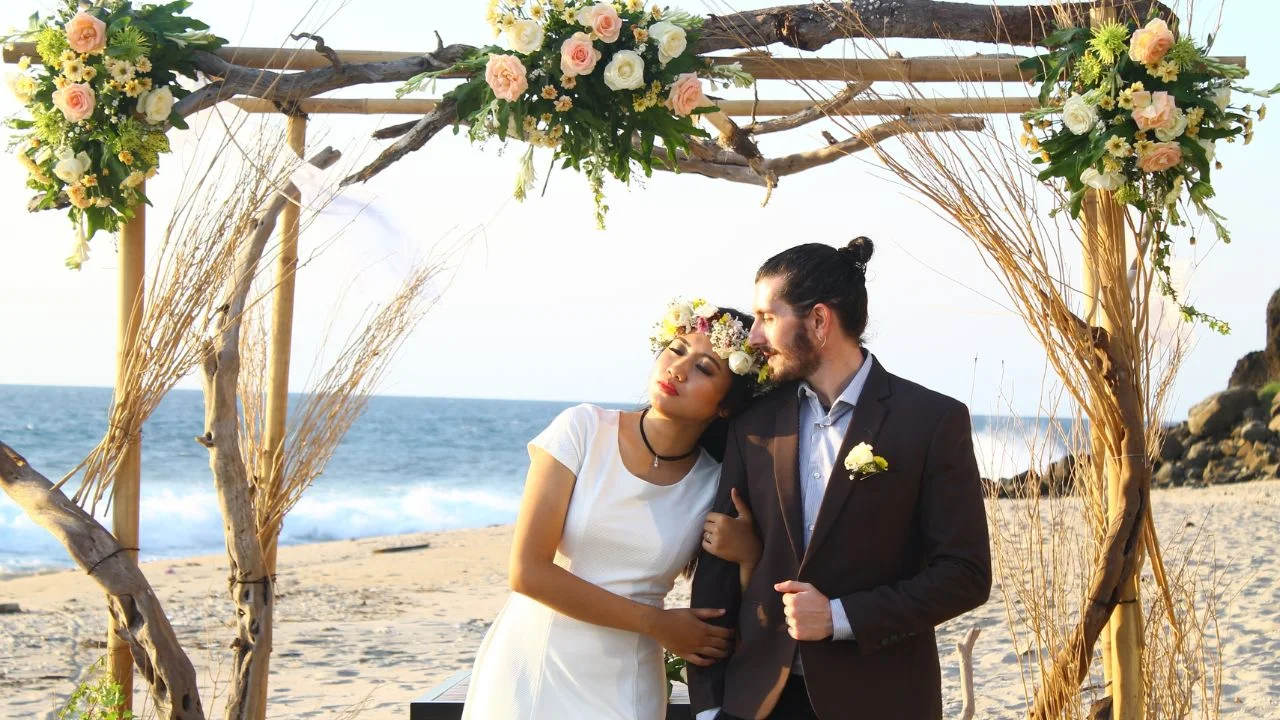 Bride and groom under a floral arch on the beach