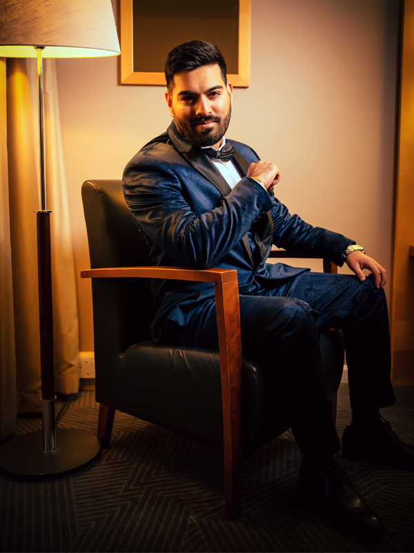 Groom posing sitting on a chair with lamp behind him.