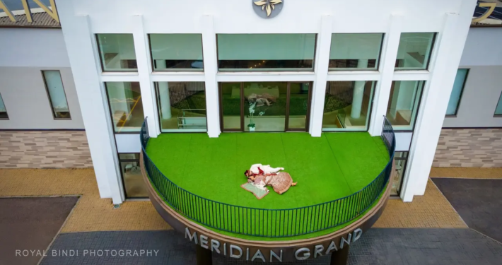 Indian bride and groom in traditional wedding attire lying on the green balcony of Meridian Grand, photographed from a top view by Royal Bindi Photography.