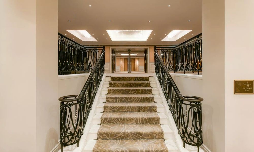 The entrance to The Portland Hotel, featuring a grand staircase with ornate railings and a carpeted runner.