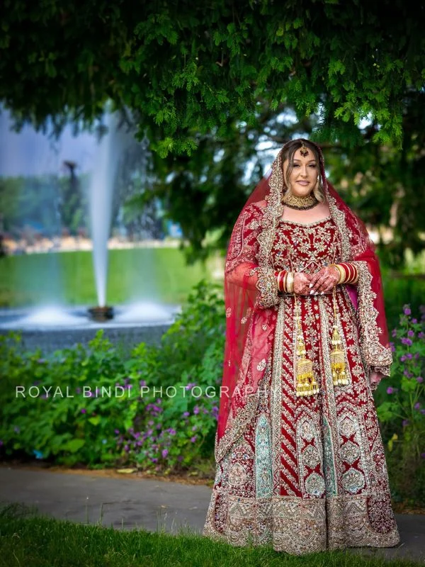 Bride in red lehenga standing by a fountain