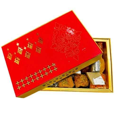 A red gift box with gold designs, filled with various Indian sweets.