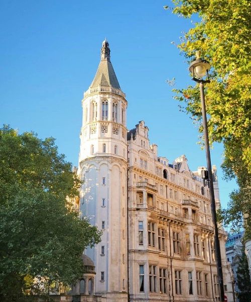 A photo of the National Liberal Club in London, England. The building features a tall tower and ornate architecture, with trees and a lamppost in the foreground.