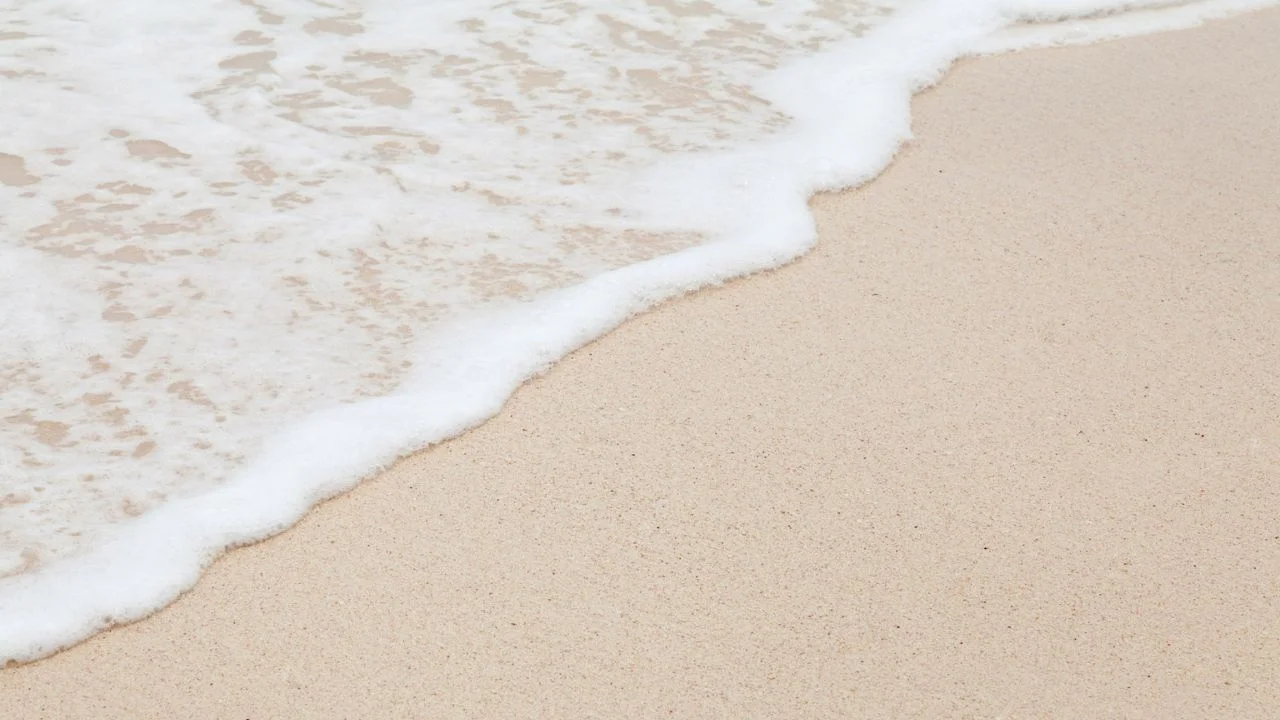 A close-up of a sandy beach with a wave lapping at the shore.