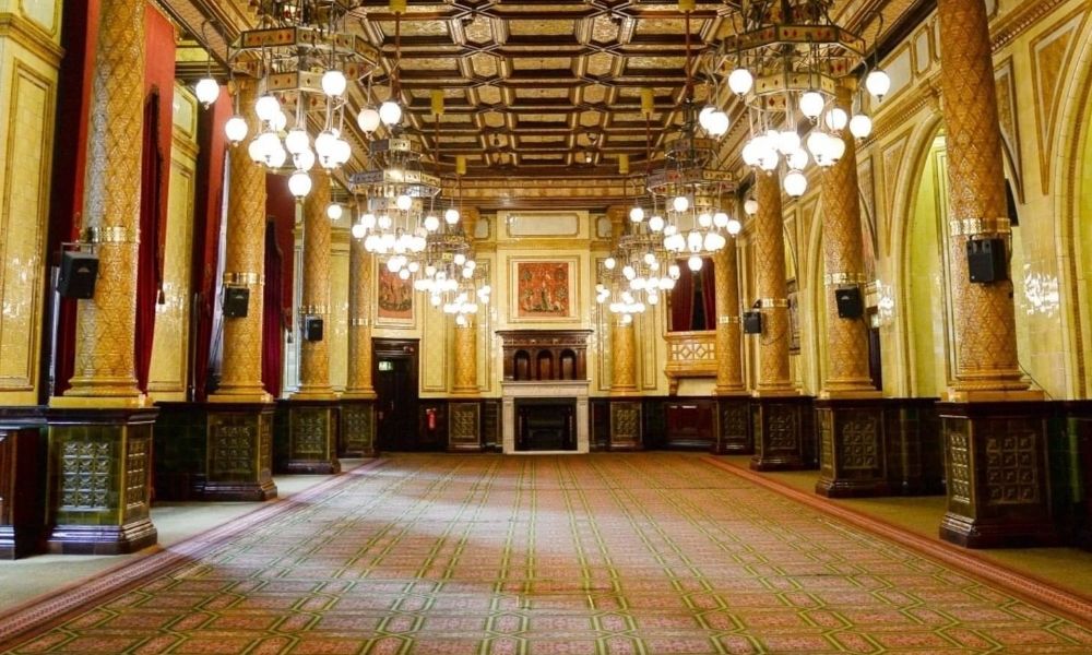 A grand ballroom with ornate columns, chandeliers, and a patterned carpet. This is likely the Great Hall at The Royal Horseguards Hotel in London.