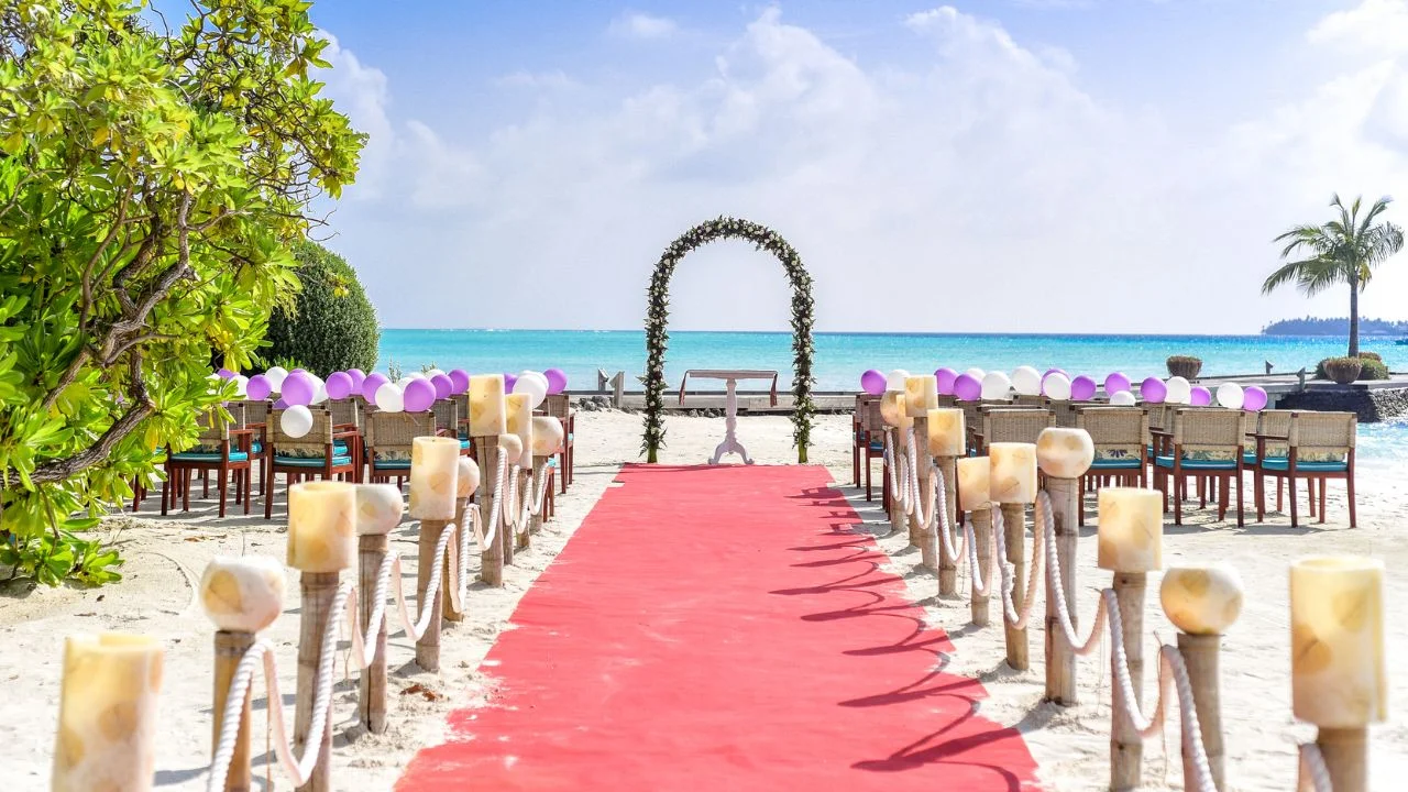 A beach wedding setup with a red carpet, floral arch, and balloons.