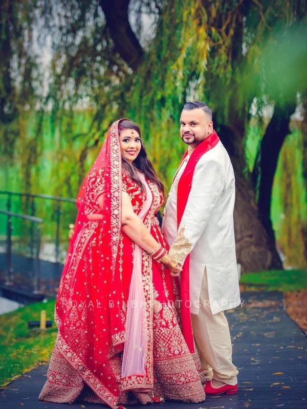 Bride and groom in red and white traditional wedding attire, holding hands outdoors.