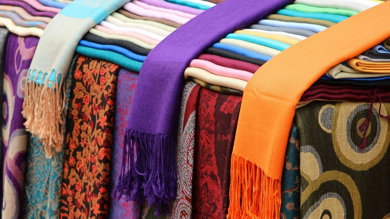 A colorful display of shawls and scarves in various patterns and colors arranged on a stall.