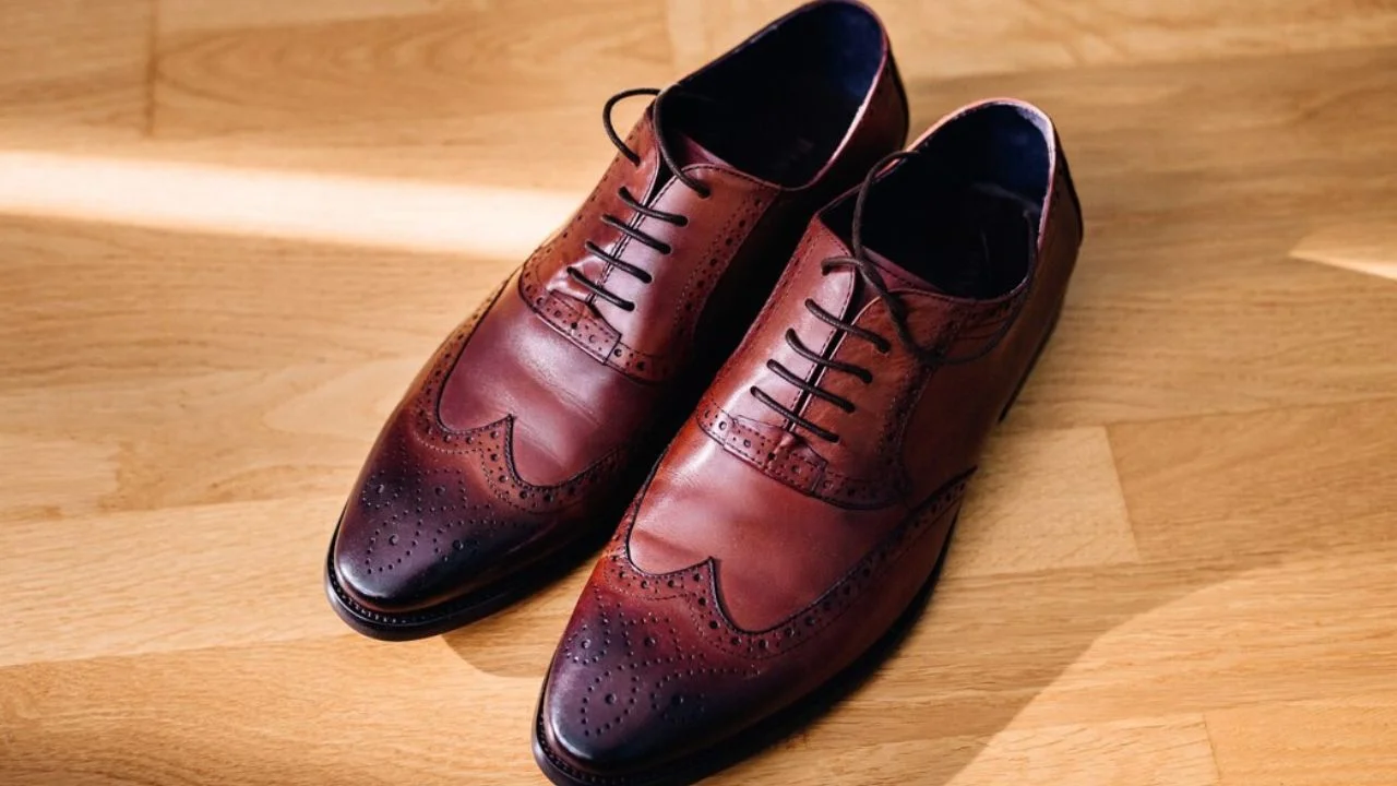 A pair of brown leather oxford shoes with laces, sitting on a wooden floor.