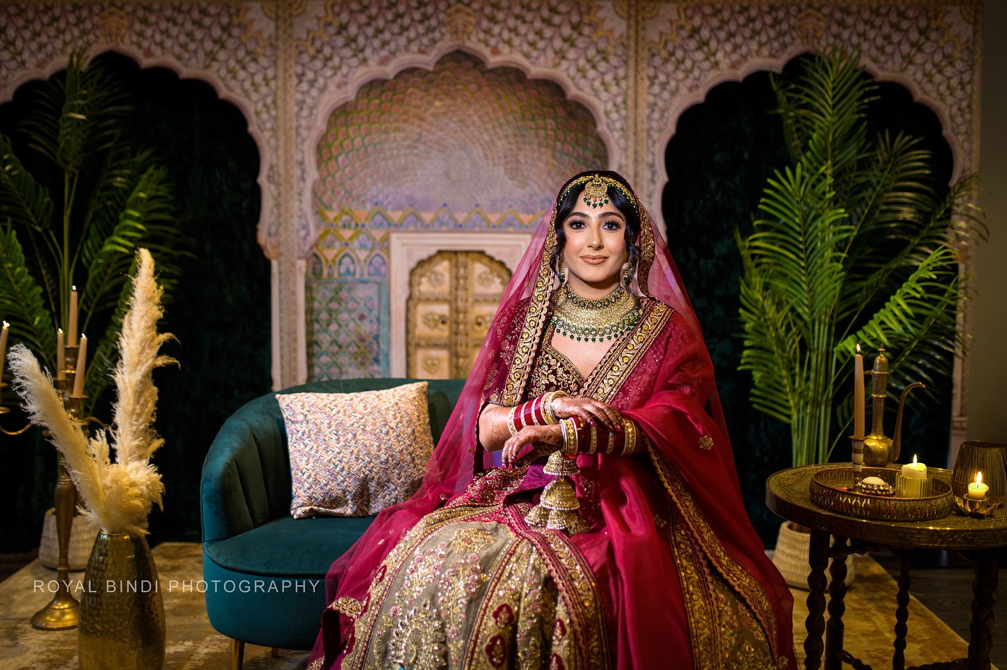 Bride in a maroon and gold bridal dress seated in a regal wedding setting