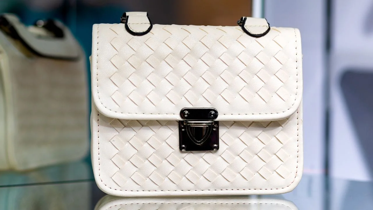 A small, white handbag with a woven leather texture and a silver clasp.