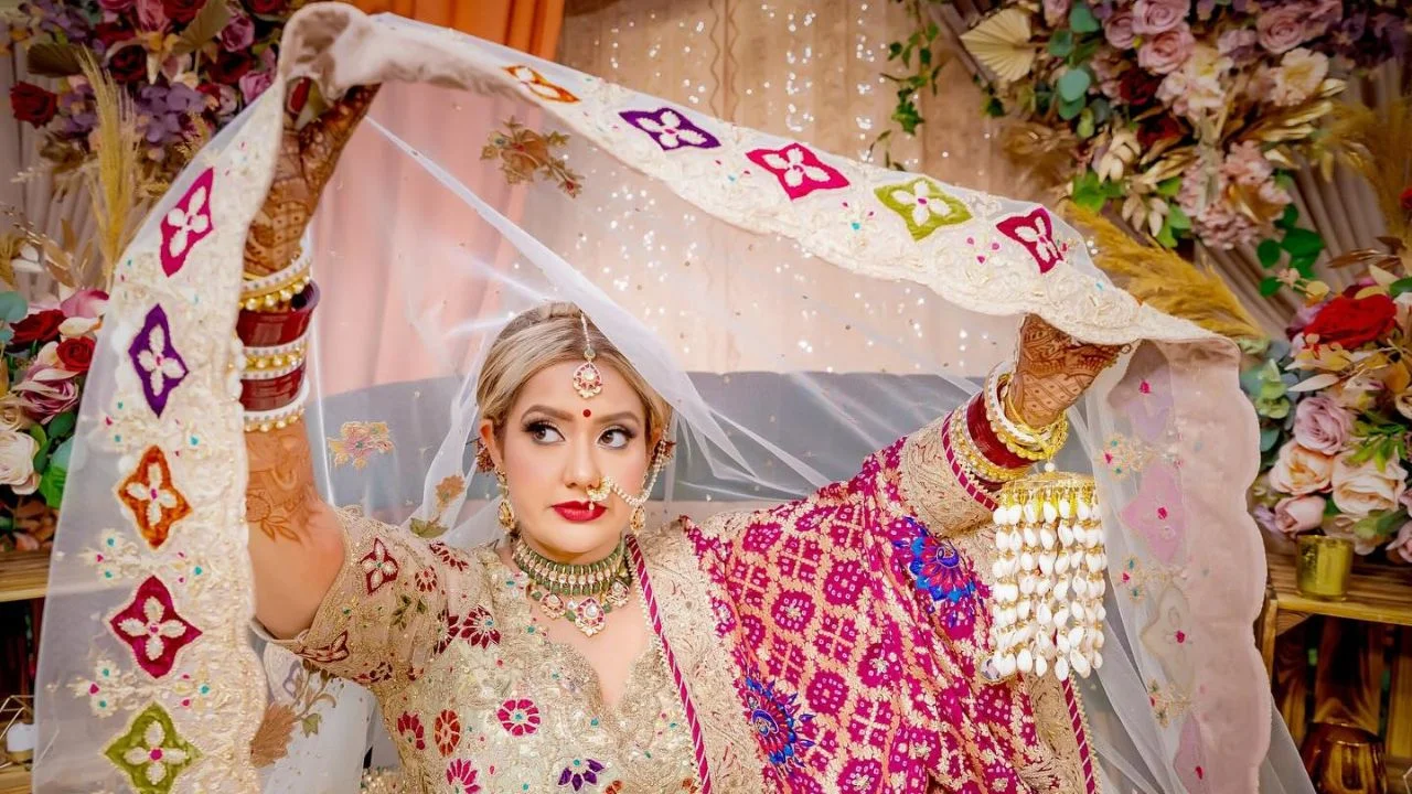 A bride in a white and gold dress, with a dupatta that has colorful embroidery around the edges.