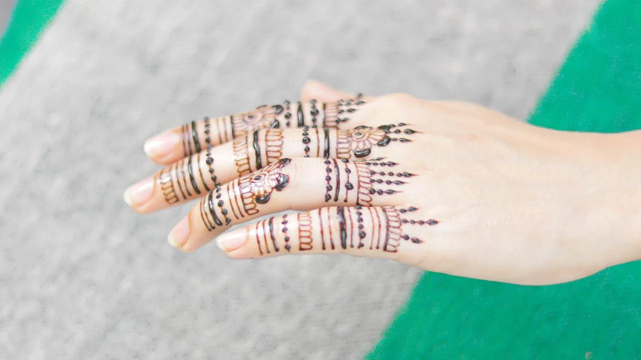 A close-up of a woman's hand with jewellery mehndi designs on her fingers.