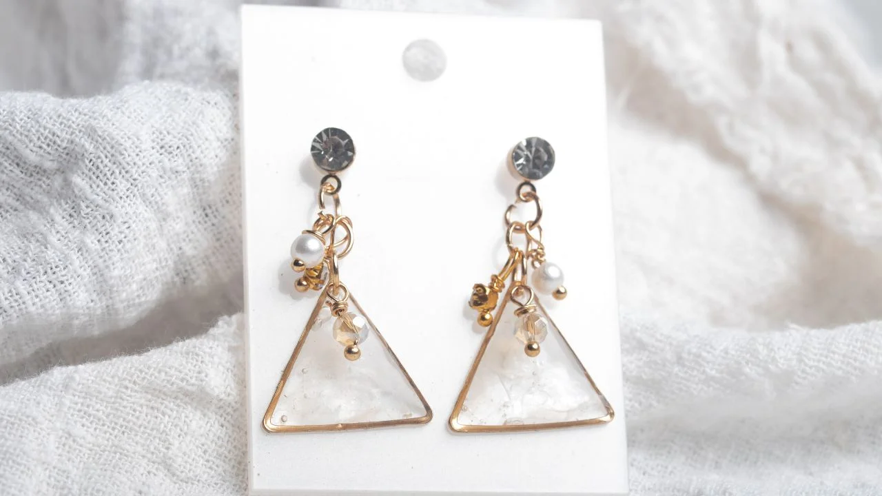 A pair of elegant earrings featuring triangular pendants adorned with gold-toned accents, pearls, and crystals.