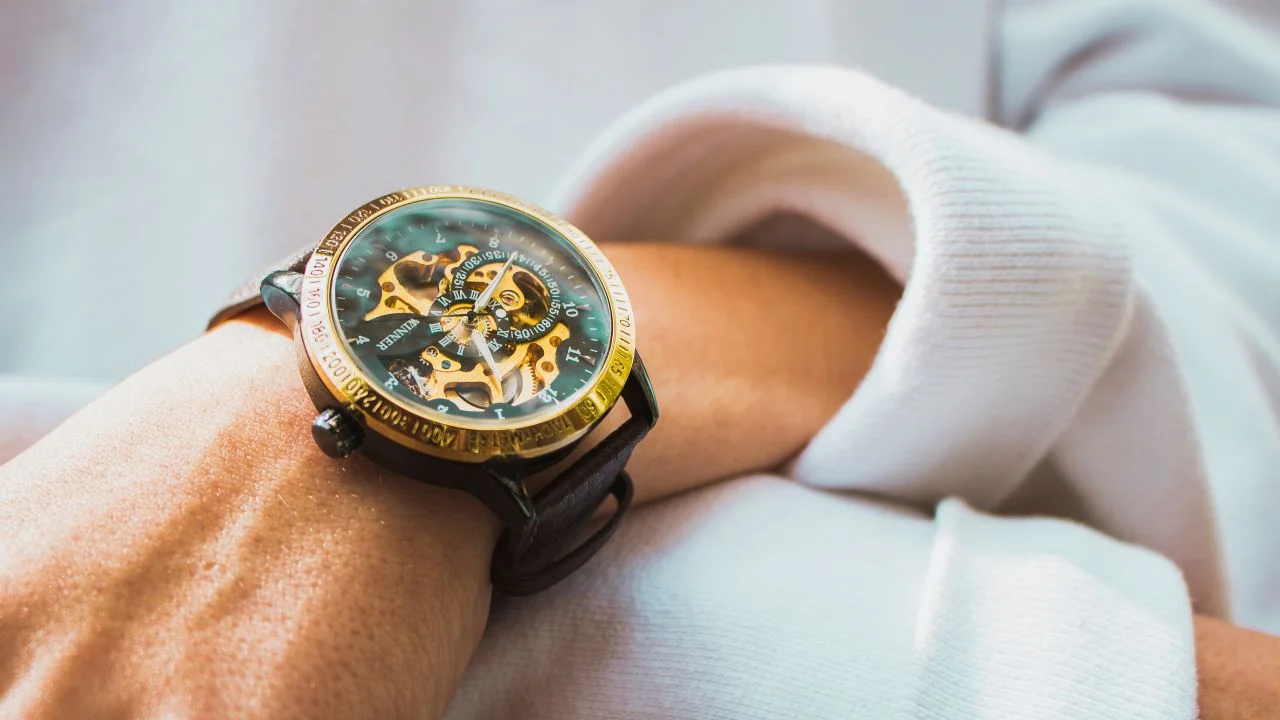 A close-up of a person wearing a gold and black skeleton watch with a visible mechanical movement.