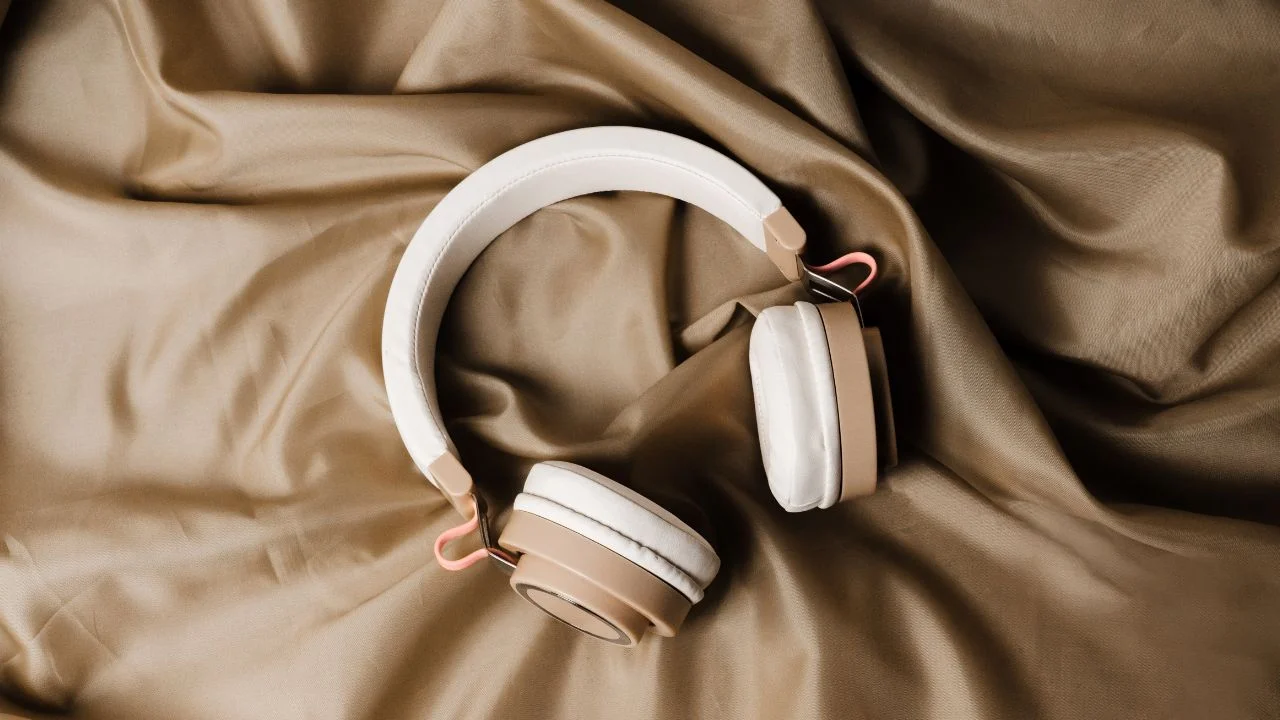 A pair of white headphones with pink accents resting on a beige fabric surface