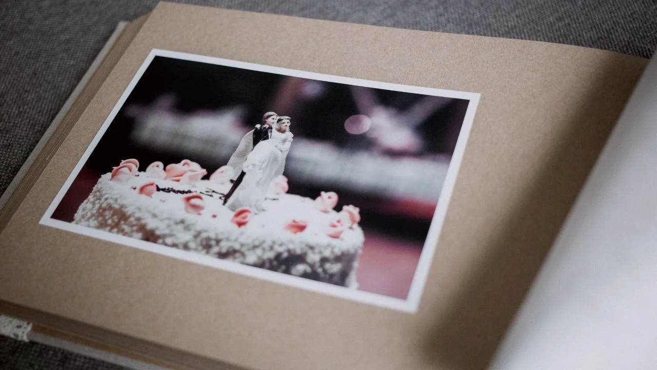 A photo of a wedding cake with a bride and groom cake topper is displayed in a brown wedding album.