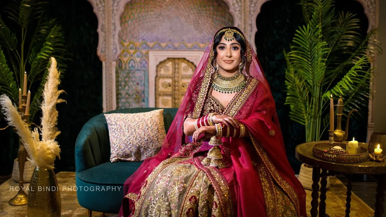 A beautiful Indian bride sitting elegantly in a red and gold lehenga.