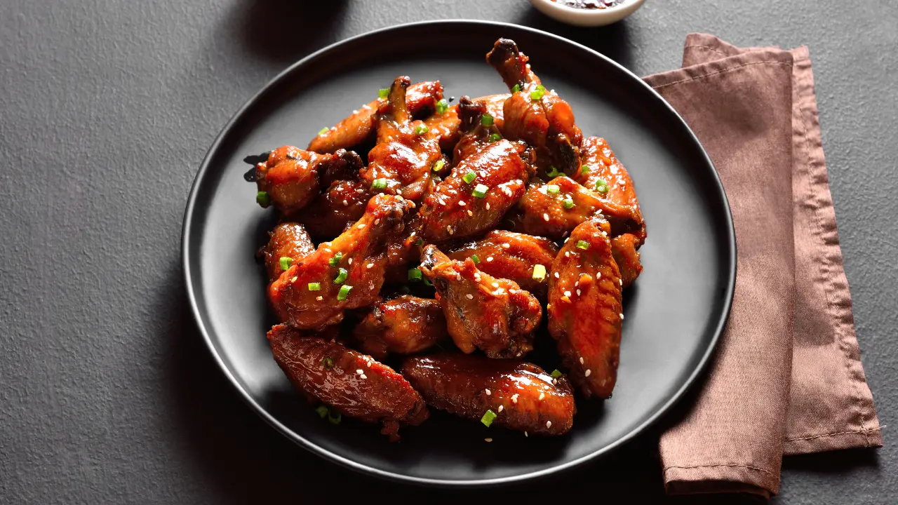 A plate of crispy chicken wings coated in a sweet and savory sesame sauce, garnished with green onions and sesame seeds.