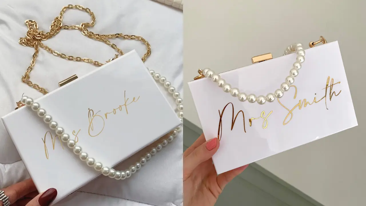 Two white acrylic clutches with gold lettering and pearl accents, personalized with the names "Mrs. Brooke" and "Mrs. Smith."