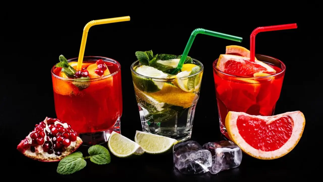 Three refreshing cocktails in glasses with colorful straws. The drinks are garnished with fruit slices and mint leaves.