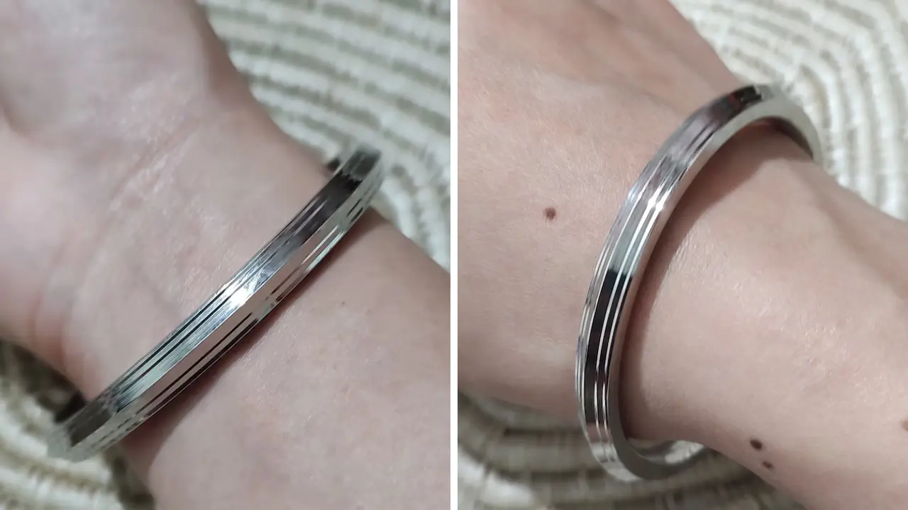 A silver bangle with a grooved design, worn on a person's wrist.